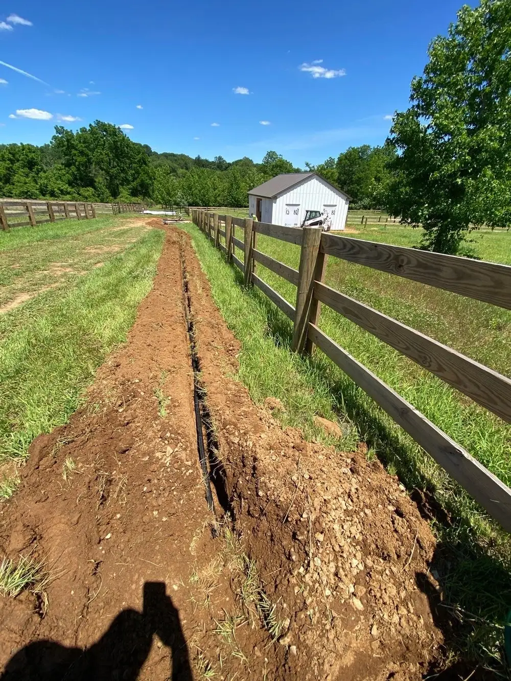 Freshly excavated drainage trench toward an outbuilding in Chester County clay soil
